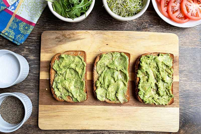 Horizontal image of avocado spread on slices of toast on a work surface.