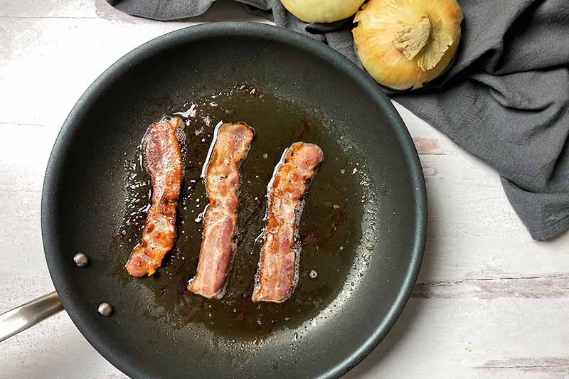 Horizontal image of cooking bacon in a skillet.