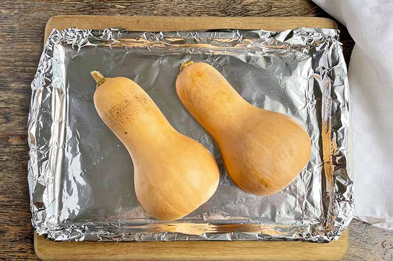 Horizontal image of roasted halves of butternut on a lined baking sheet.
