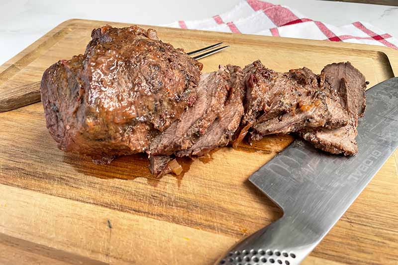Horizontal image of slicing a browned chuck roast on a wooden cutting board.