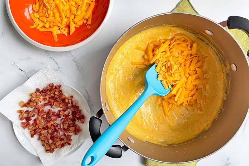 Horizontal image of mixing shredded cheddar in a pot of sauce.