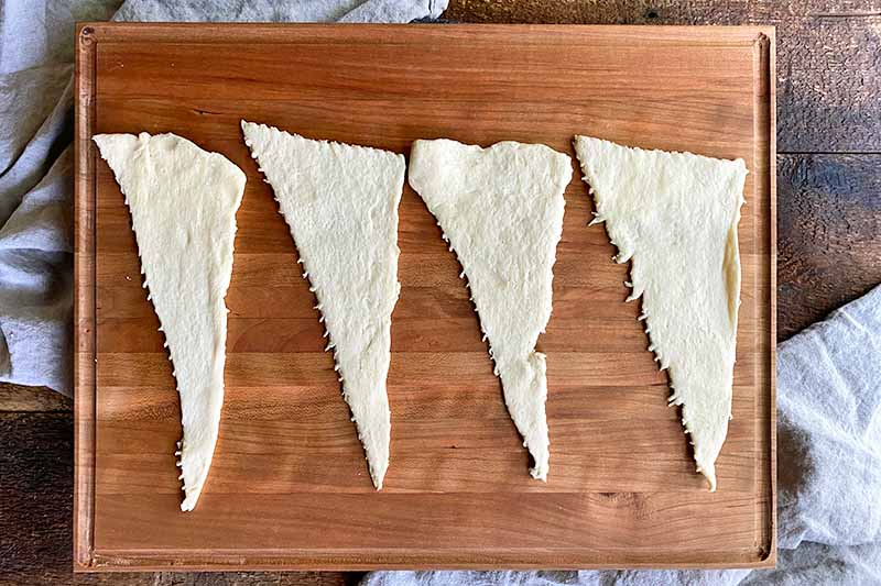 Horizontal image of four triangular pieces of raw dough on a wooden board.