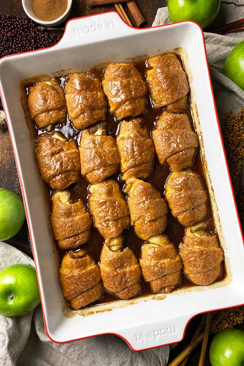 Vertical image of baked pastries in neat rows in a baking dish with a spiced sauce.