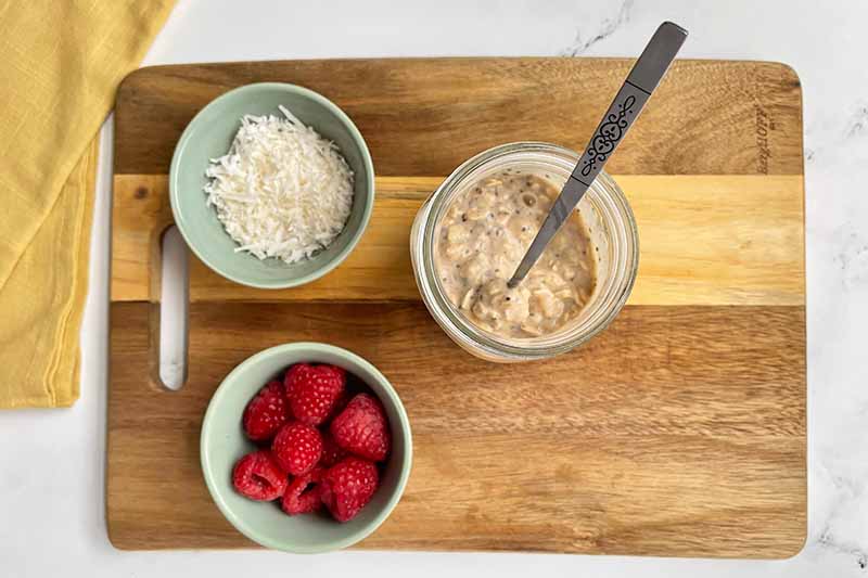 Horizontal image of oatmeal in a jar next to bowls of toppings.