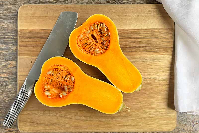Horizontal image of a halved butternut on a wooden board next to a knife.