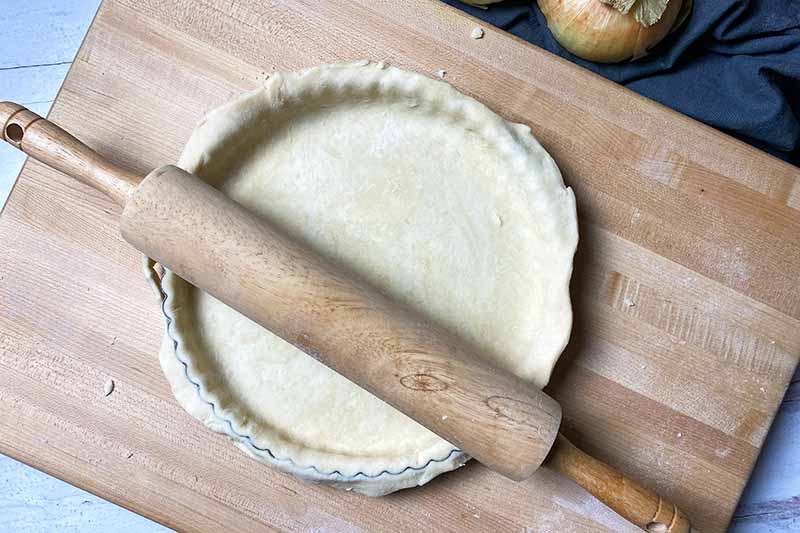 Horizontal image of cutting off excess dough from a pan with a rolling pin.