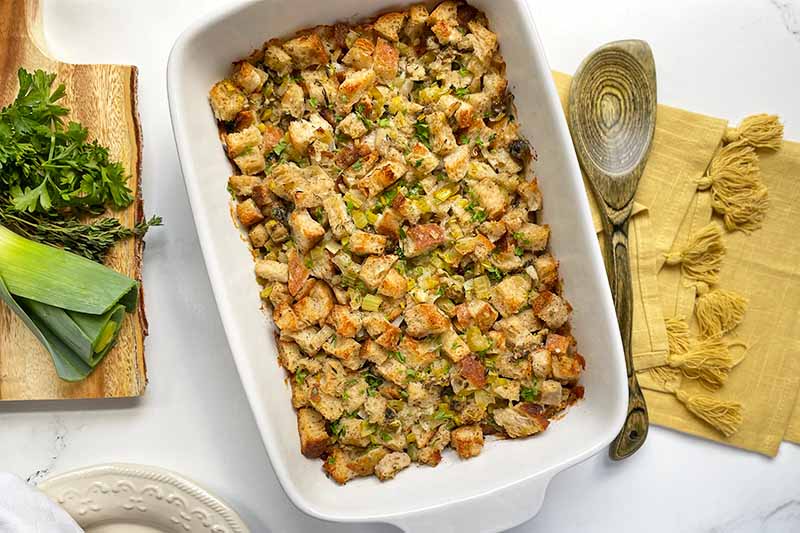 Horizontal image of a baked casserole dish full of stuffing next to a yellow towel.
