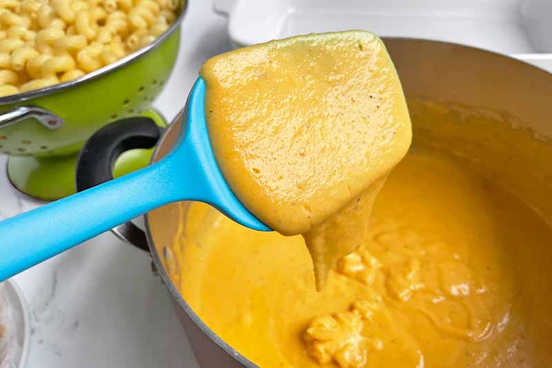 Horizontal image of mixing a creamy orange sauce with a blue spatula.