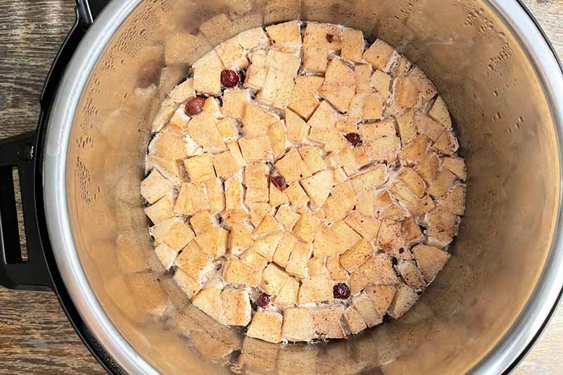 Horizontal image of cooked cubes of apples over a mixture in a slow cooker insert.