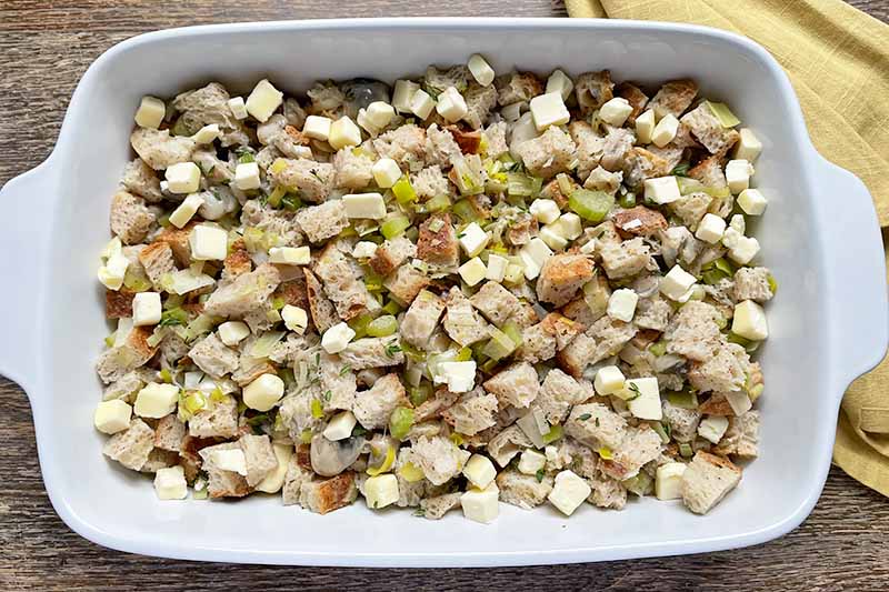 Horizontal image of an unbaked stuffing dish in a casserole with cubes of butter.