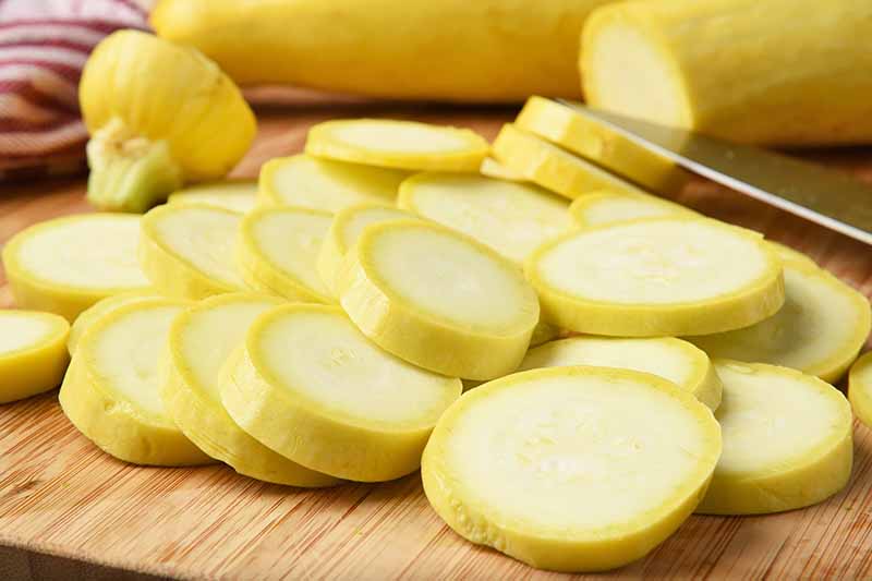 Horizontal image of sliced yellow squash on a wooden cutting board.