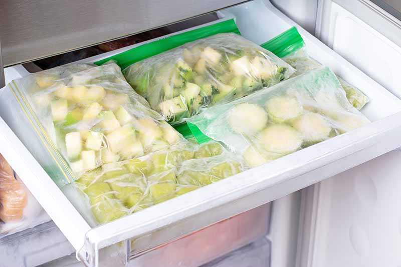 Horizontal image of frozen vegetables in assorted preparations in bags in the freezer drawer.