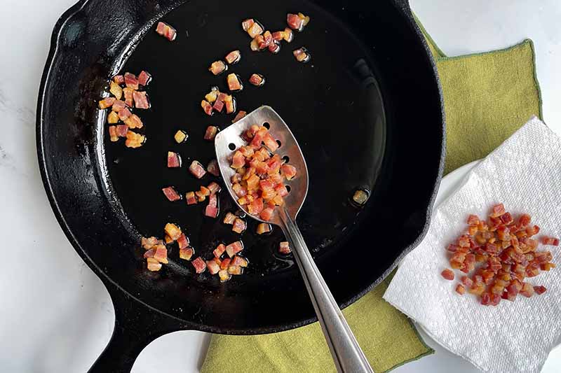 Horizontal image of cooking cubes of pancetta in a cast iron skillet.
