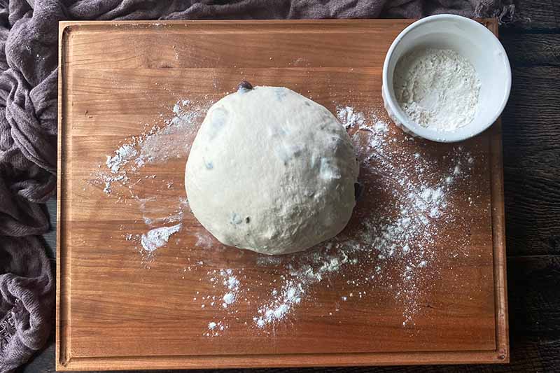 Horizontal image of a flavored round of dough next to a bowl of flour.