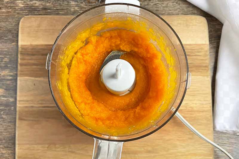 Horizontal image of a smooth orange mixture in a food processor.