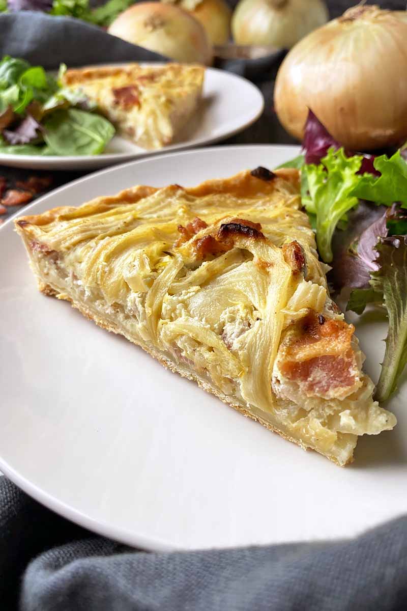 Vertical image of a slice of savory pie on a plate next to salad greens.