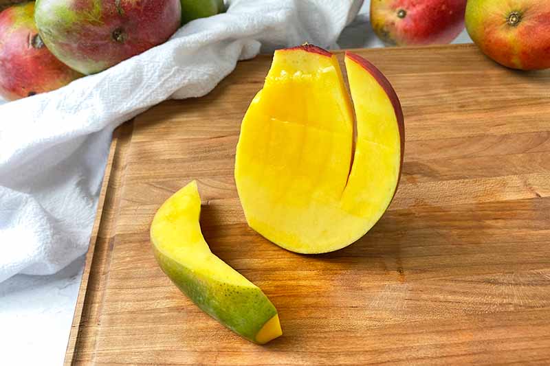 Horizontal image of slicing long pieces from a mango.