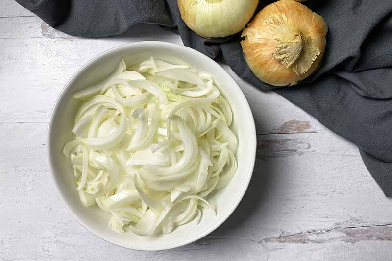 Horizontal image of sliced onions in a bowl.