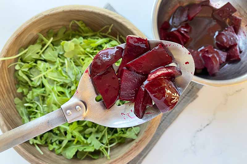 Horizontal image of marinated beets over a wooden bowl filled with lettuce.