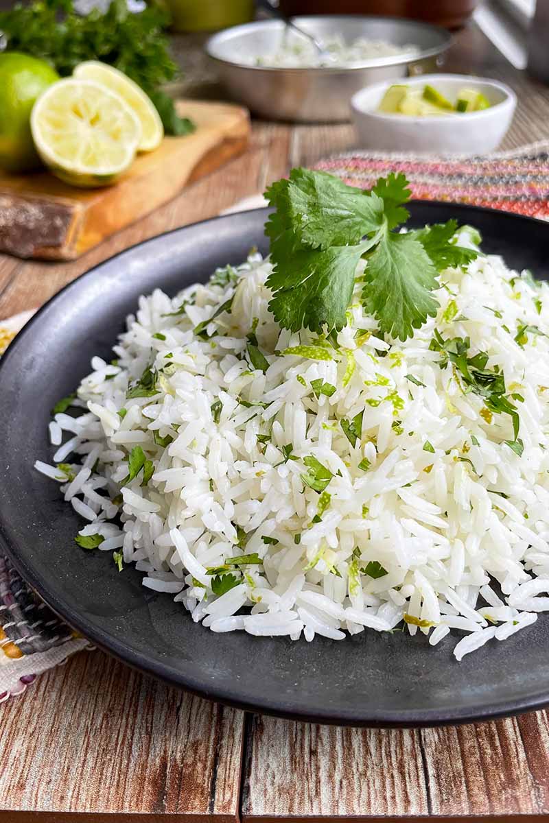 Vertical close-up image of a black plate topped with a mound of rice mixed with citrus zest and herbs on a wooden table.