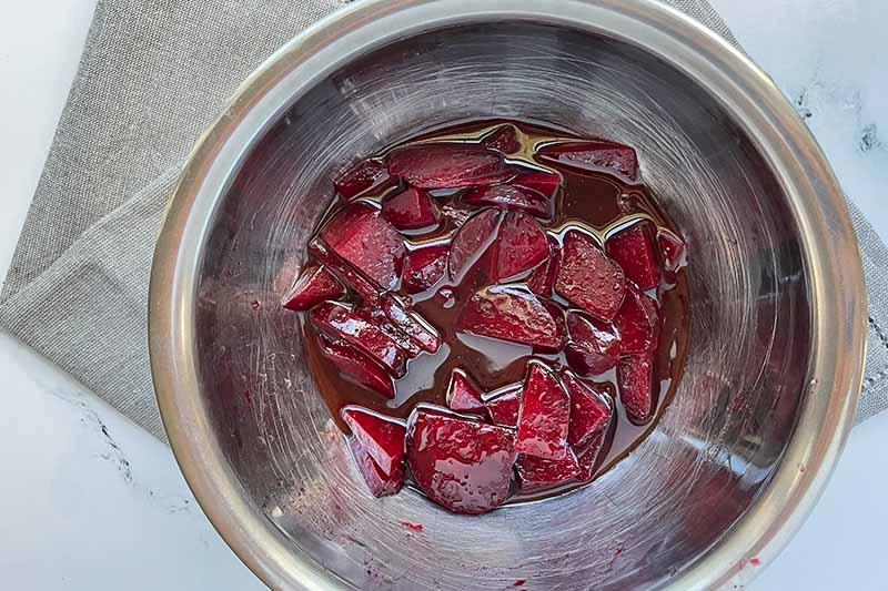 Horizontal image of marinated chopped beets in a metal bowl.