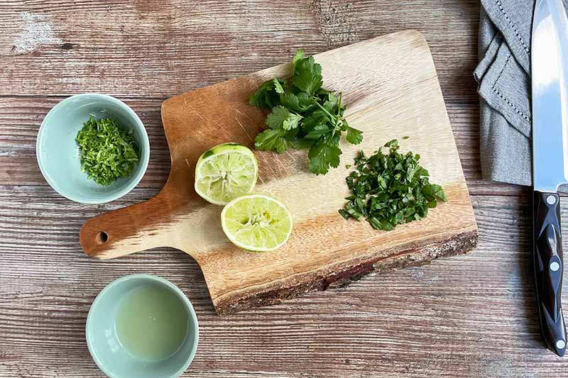 Horizontal image of juiced limes and chopped cilantro on a wooden cutting board.