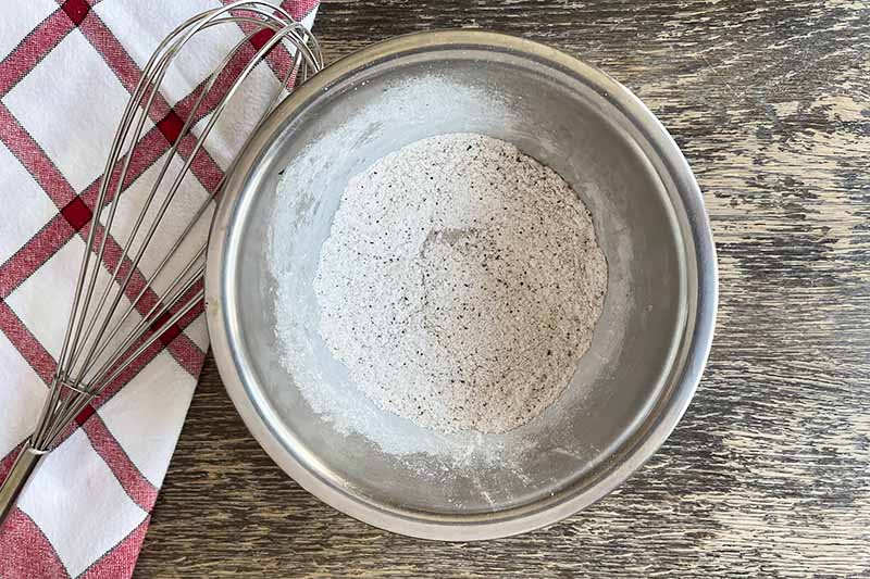 Horizontal image of a seasoned flour mixture next to a whisk.