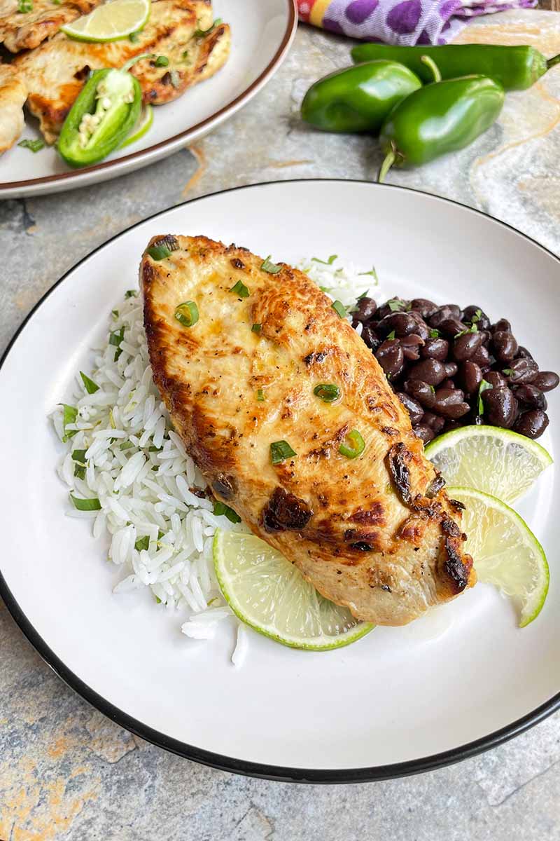 Vertical image of a seared piece of poultry on top of rice and beans with lime wedges.