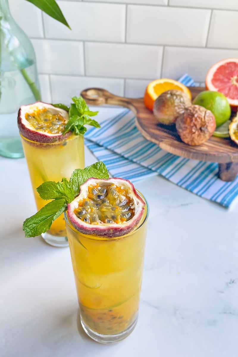 Vertical image of two glasses filled with bright yellow drinks topped with assorted fresh garnishes.