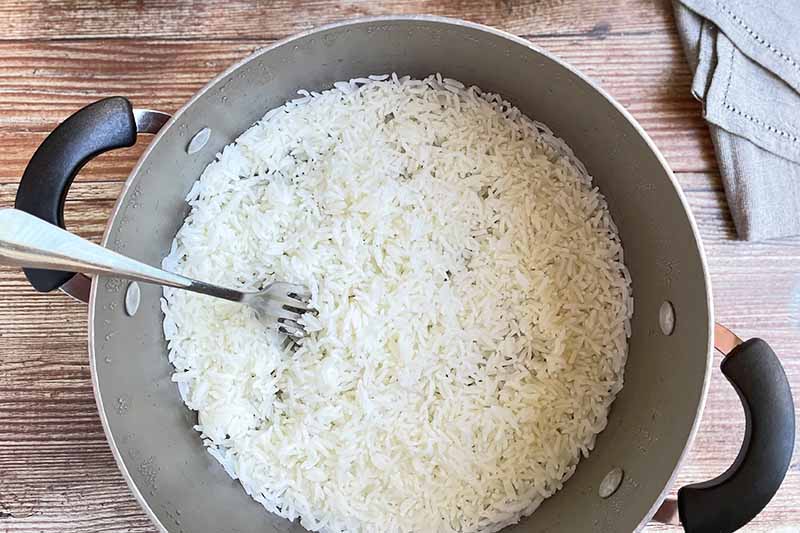 Horizontal image of fluffing cooked white grains with a fork in a pot.