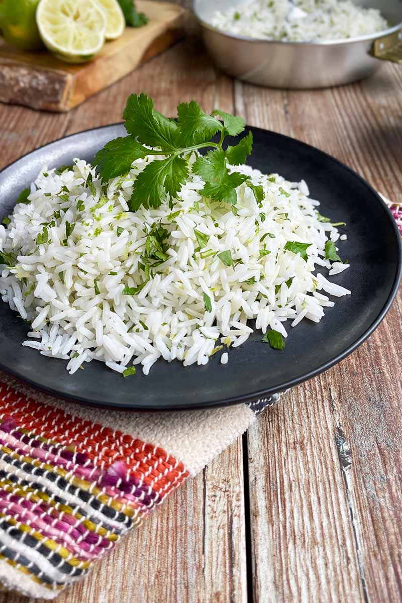 Vertical image of a black plate with herbed rice on a colorful towel.