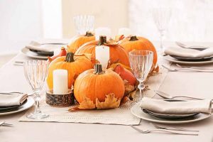 Horizontal image of a dining table covered in tablecloth with pumpkin and candle centerpieces.