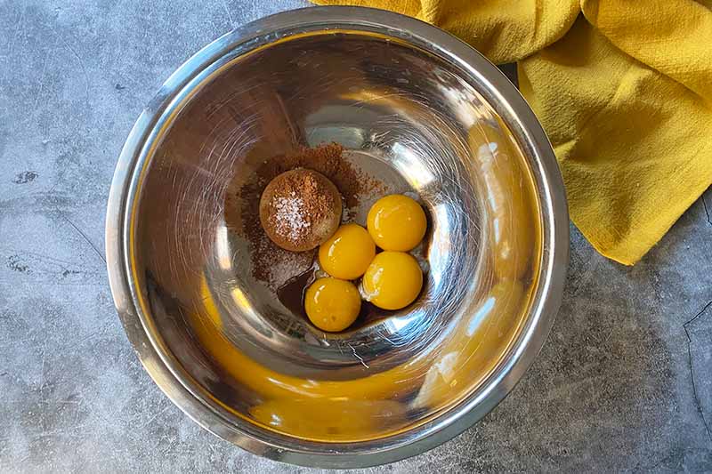 Horizontal image of egg yolks, salt, and brown sugar in a metal bowl.