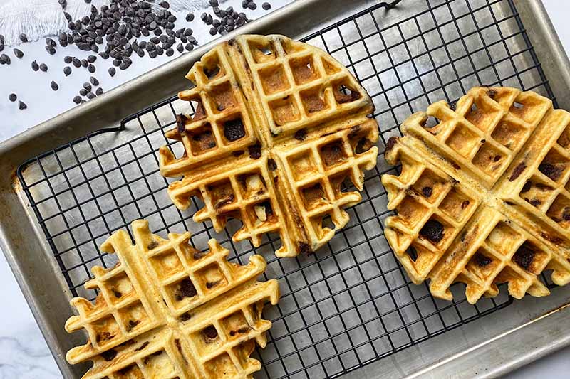 Horizontal image of three waffles on a baking sheet with a cooling rack.