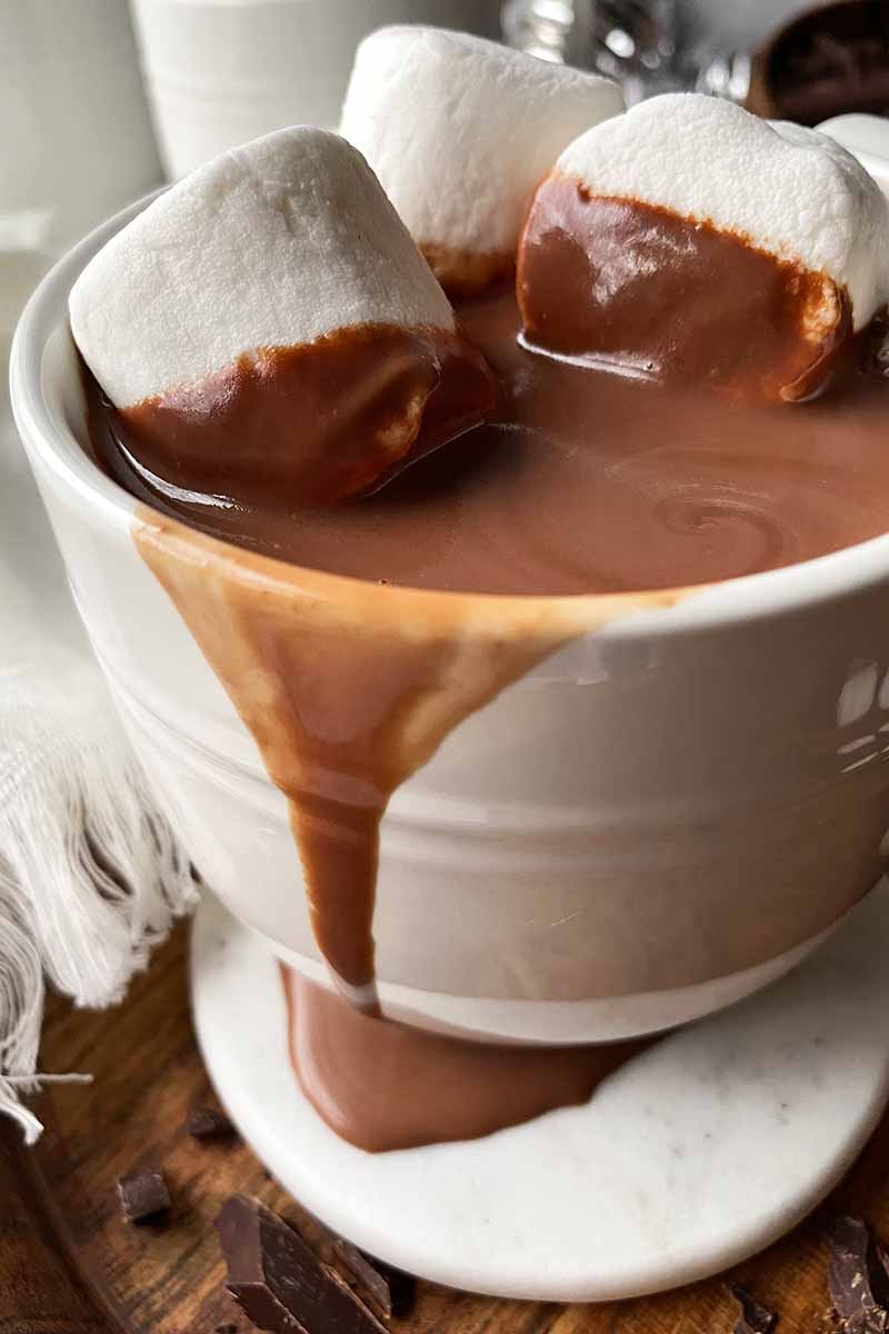 Vertical image of a messy mug with a creamy dark brown beverage topped with marshmallows.