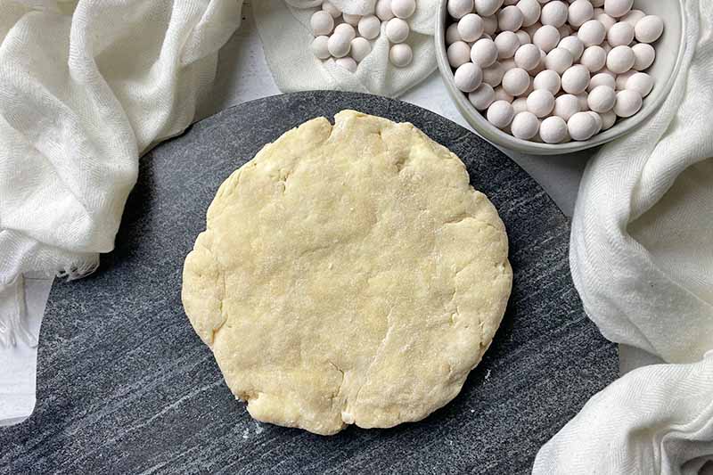 Horizontal image of a disc of dough on a gray cutting board.