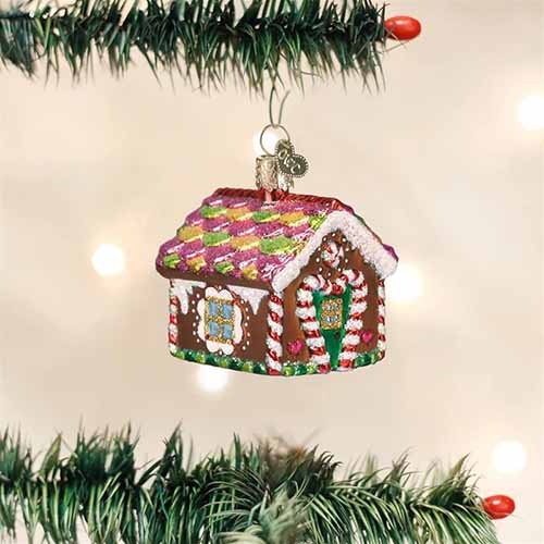 Image of a small gingerbread house ornament hanging from the branches of a tree.