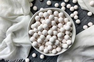 Horizontal image of a bowl filled with white ceramic balls next to a white towel.