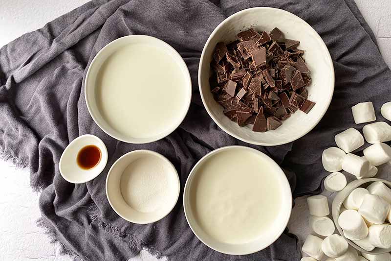 Horizontal image of sugar, milk, vanilla, and chopped candy prepped and measured in white bowls.