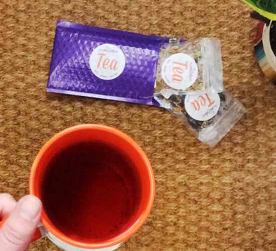 Image of a hand holding a cup of tea next to Plum Deluxe packages.