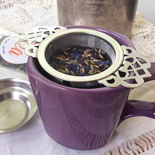 Image of a Plum Deluxe metal tea infuser over a cup of tea.