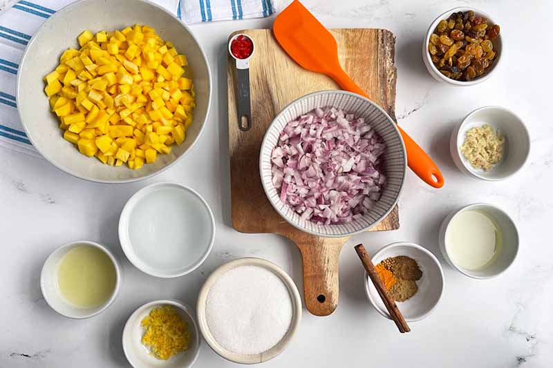 Horizontal image of assorted prepped, measured, and chopped ingredients in different sized bowls next to an orange rubber spatula.
