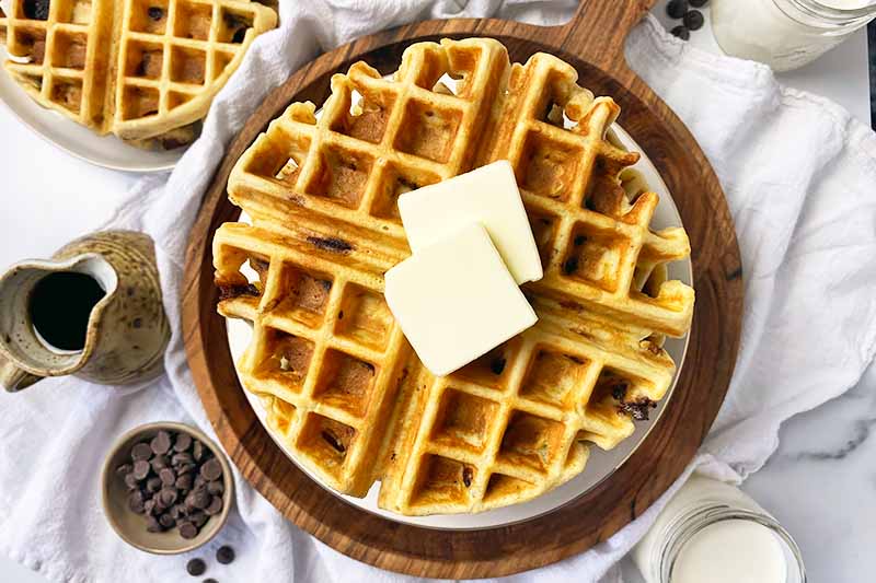 Horizontal image of waffles topped with butter over a white towel.
