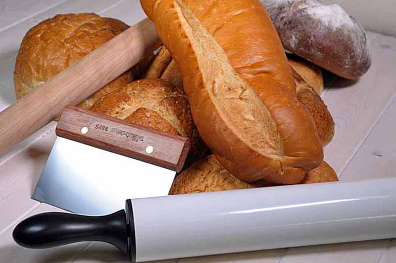 Horizontal image of assorted baked goods next to a rolling pin and bench scraper.