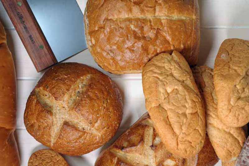 Horizontal image of assorted baked goods next to a bench scraper with a wooden handle.