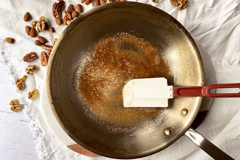 Horizontal image of toasting seasonings in oil in a skillet stirred by a rubber spatula.