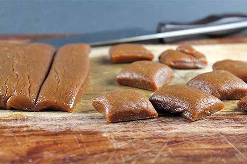 Horizontal image of cutting squares of homemade caramel on a wooden cutting board.