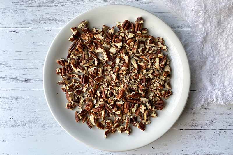 Horizontal image of chopped toasted pecans on a white plate.