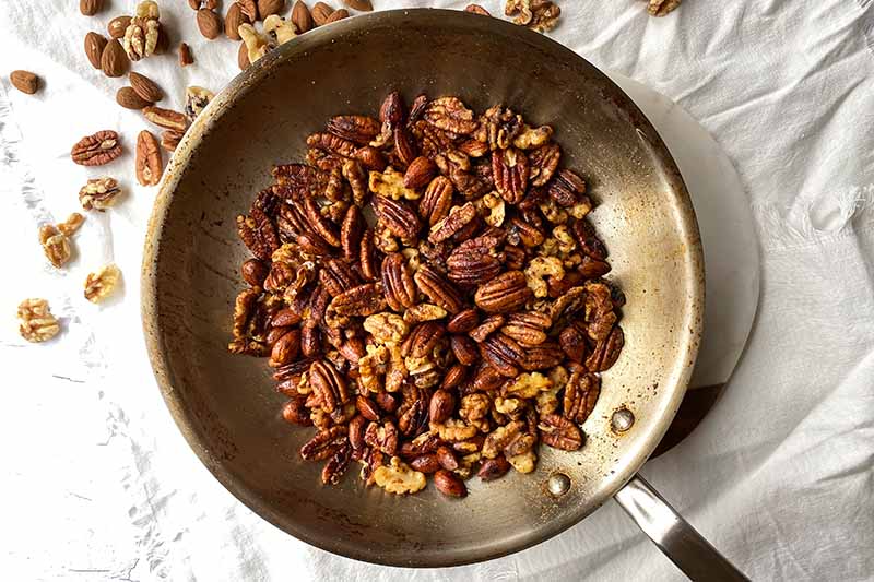 Horizontal image of a seasoned pecan and almond mix in a skillet.