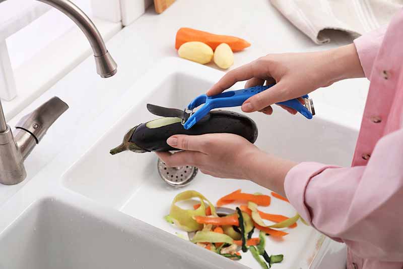 Horizontal image of peeling vegetables over a sink.
